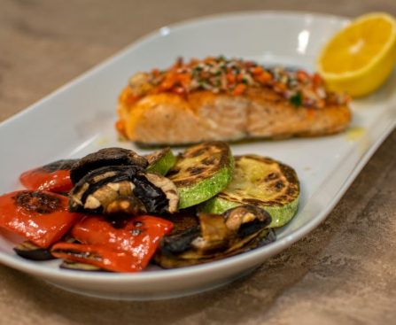 A delicious grilled salmon fillet with roasted vegetables served on a white plate.